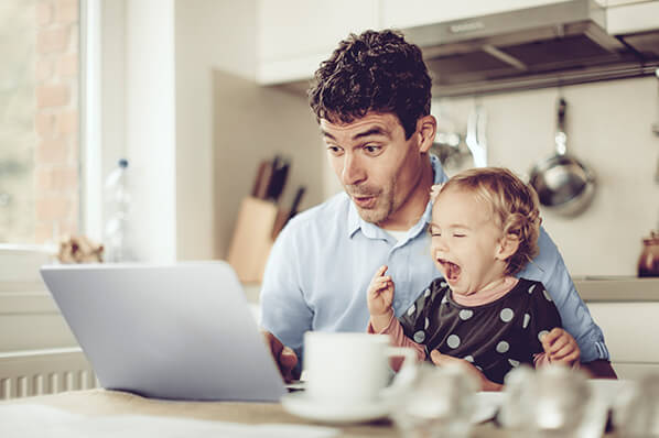 A father and this toddler at a table staring into a laptop