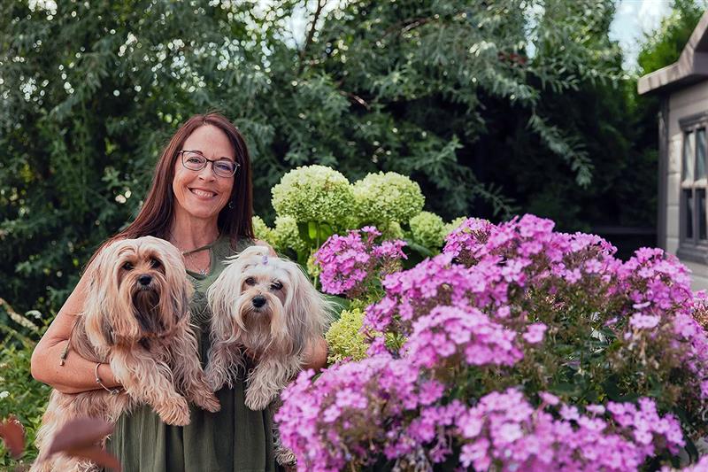 A woman holding two dogs next to flowers