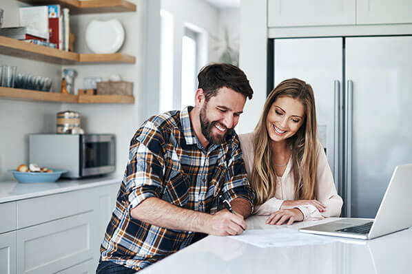 A man and a woman at a kitchen counter writing on a piece of paper