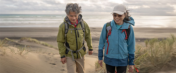 man and woman walking on the beach in light jackets