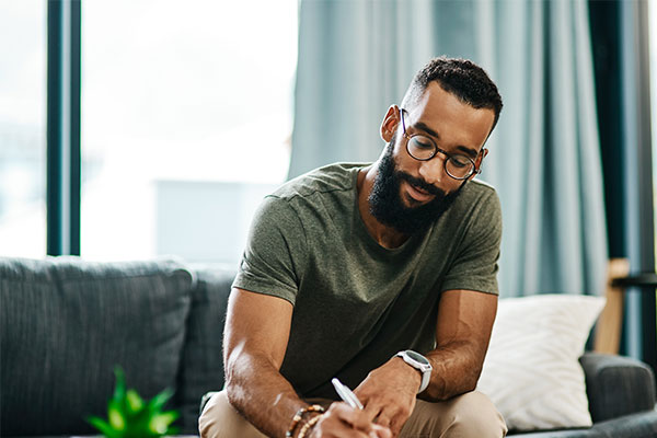 A man sitting on a couch writing on a paper