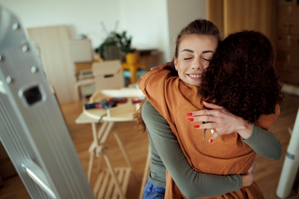 two young women hugging each other in their new home
