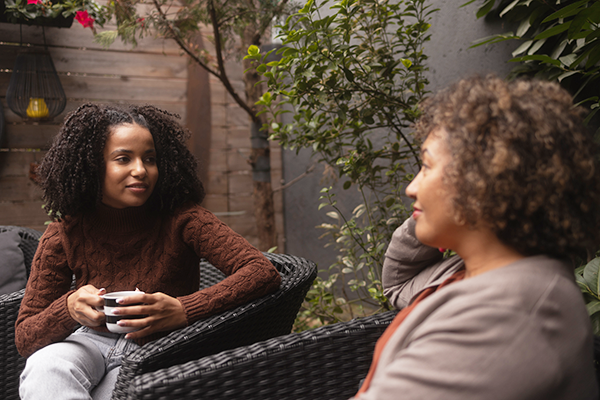 Two women seated on a patio chatting over coffee