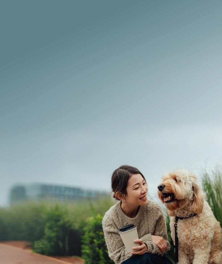 An Asian woman in her 30s leaning in to speak to her fluffy white dog